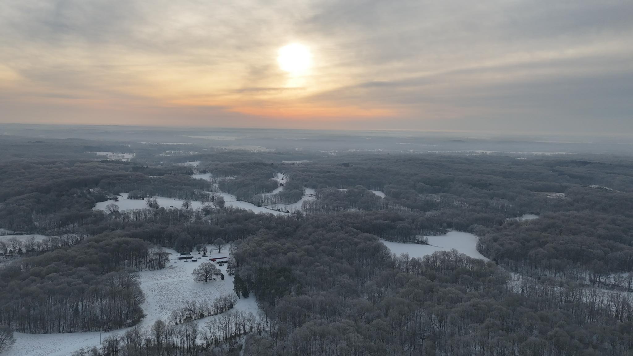 Aerial sunrise view of snow-covered rural land and wooded acreage in Beech Bluff Tennessee after a winter ice storm