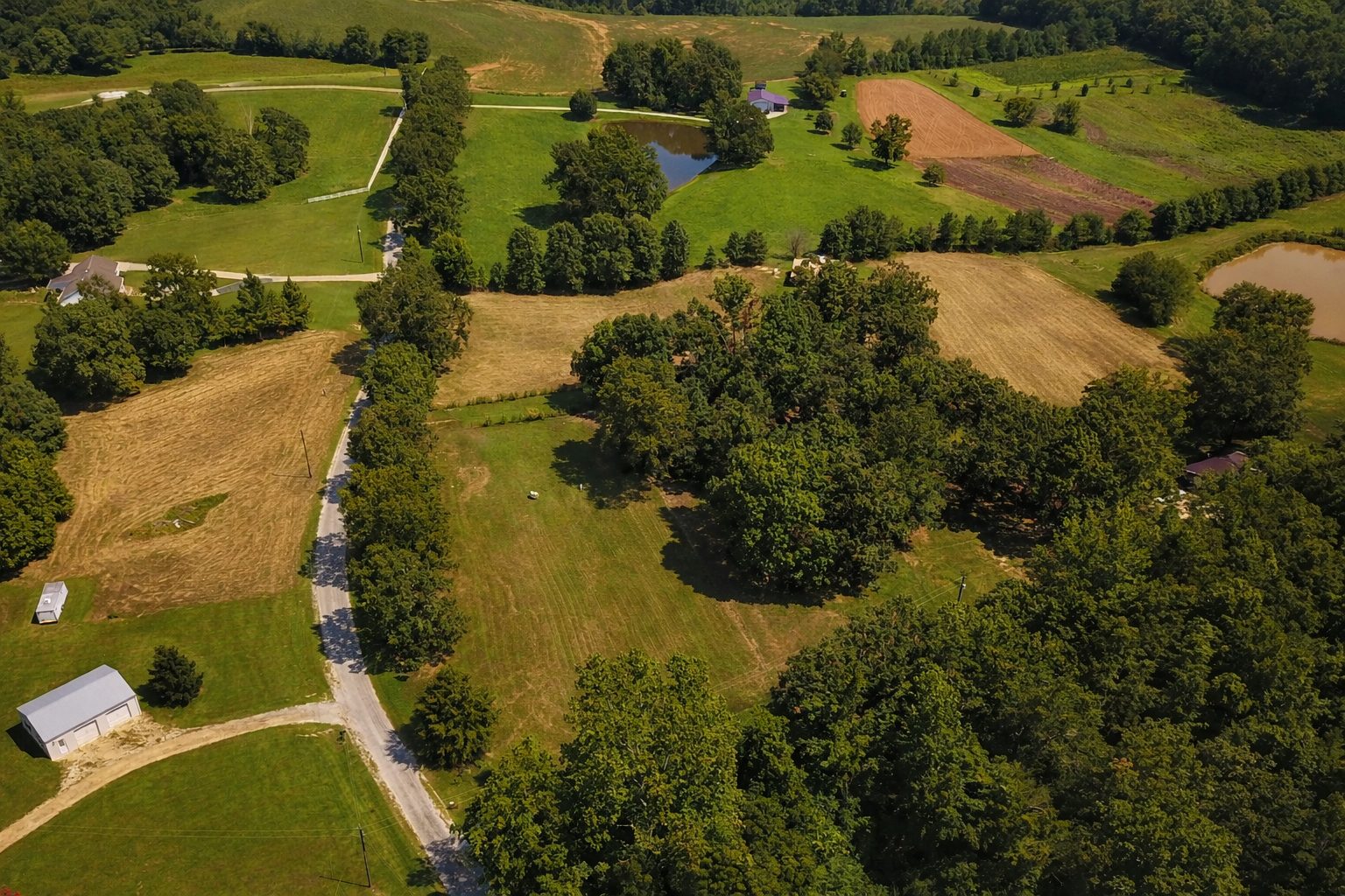 Aerial view of rural acreage and country property in West Tennessee near Beech Bluff with ponds, farmland, and tree-lined driveway.