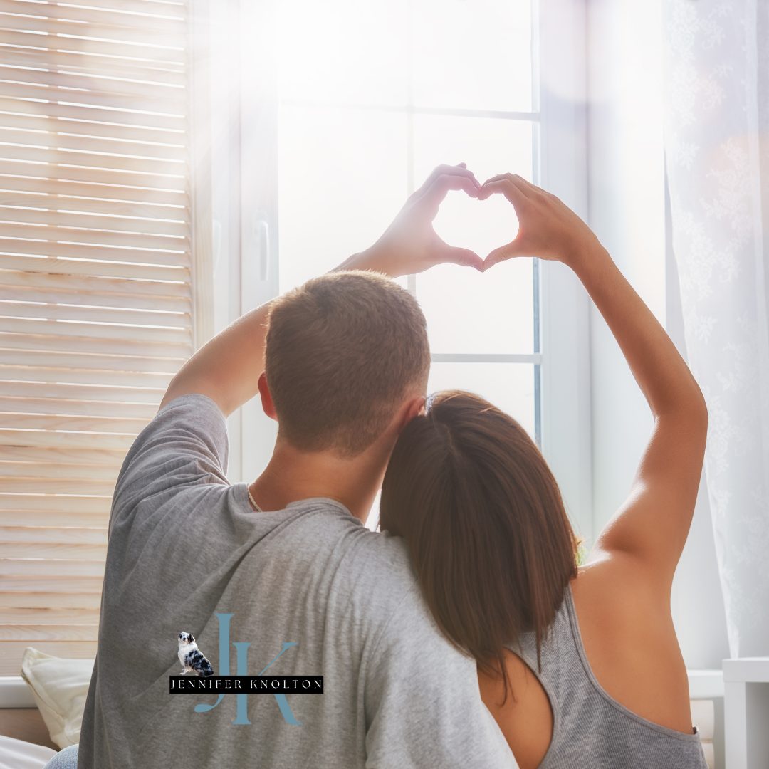 Couple looking out a bright window forming a heart with their hands, representing loving where you live in West Tennessee